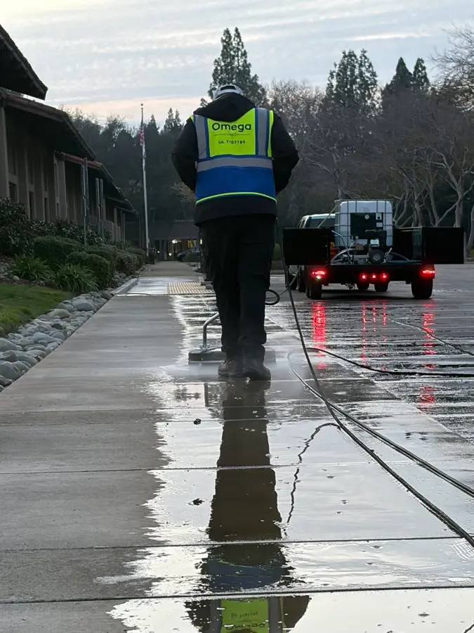 Omega crew member pressure-washing a long sidewalk